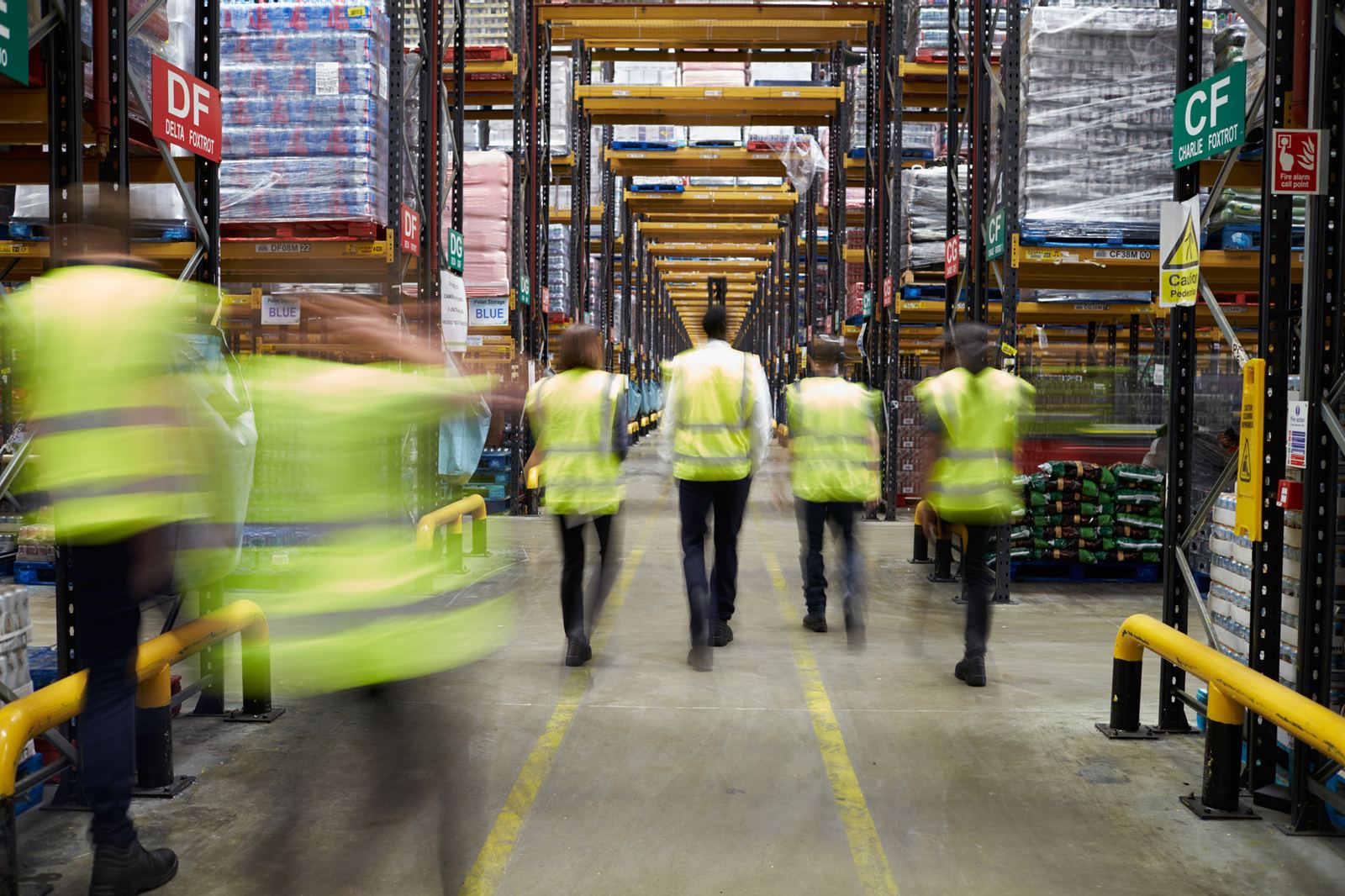 People in hi-vis walking in single file through a warehouse, seen from behind