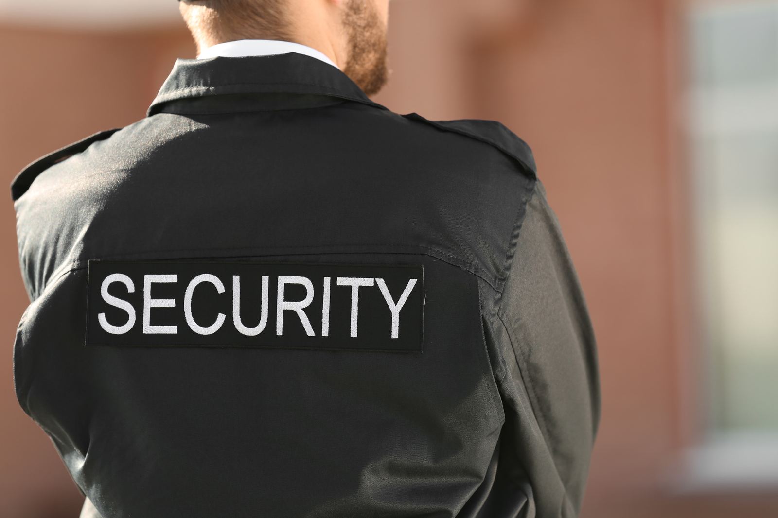 A security officer in a jacket marked SECURITY, seen from behind